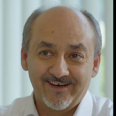 Porträt von Prof. h.c. mult. Dr. med. Amir-Mobarez Parasta: lächelnder Mann mit grauem Haar und Vollbart in weißem Hemd im Beratungsgespräch